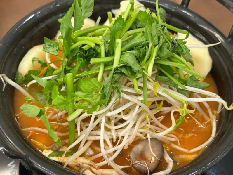 Pot full of spicy broth with minari, bean sprouts, and mushrooms