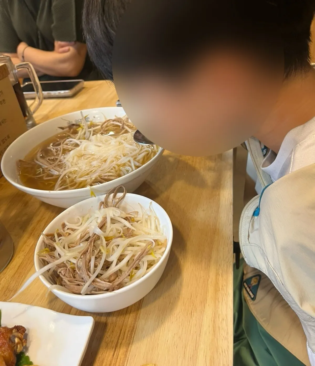 A child eating pho in front of a large bowl