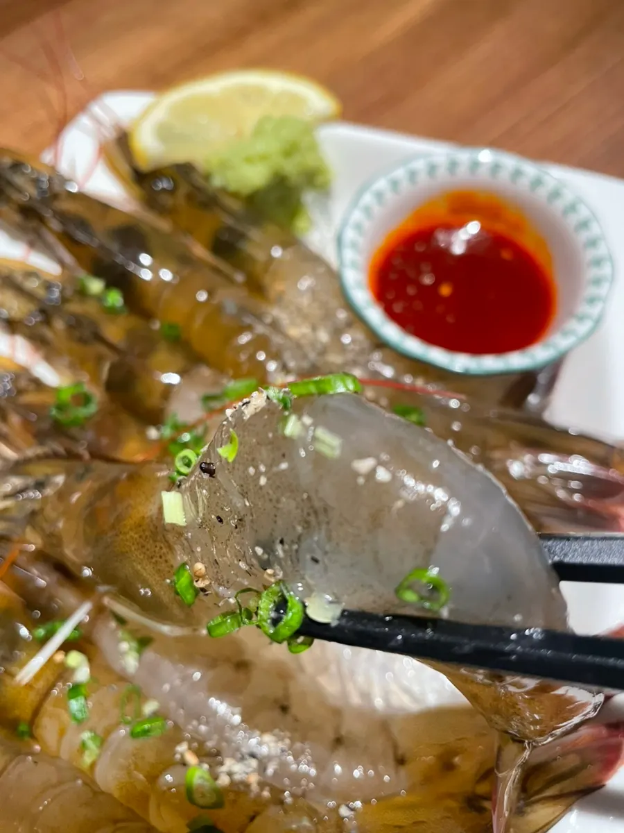 A piece of raw shrimp sashimi held up close