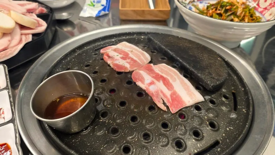 Pork belly cooking alongside seasoned scallion salad