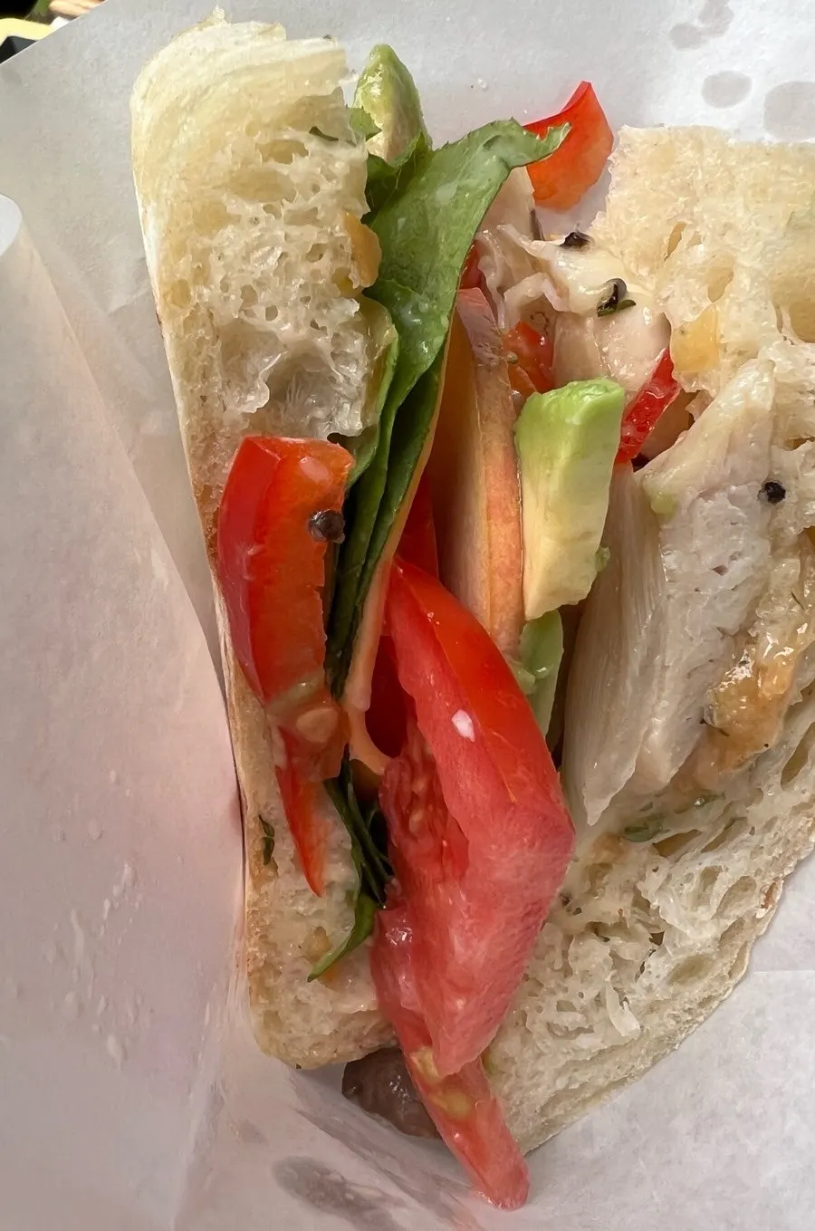 A bitten avocado chicken ciabatta sandwich