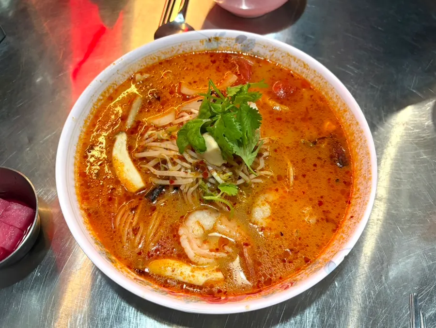 A bowl of tom yum rice noodles loaded with toppings