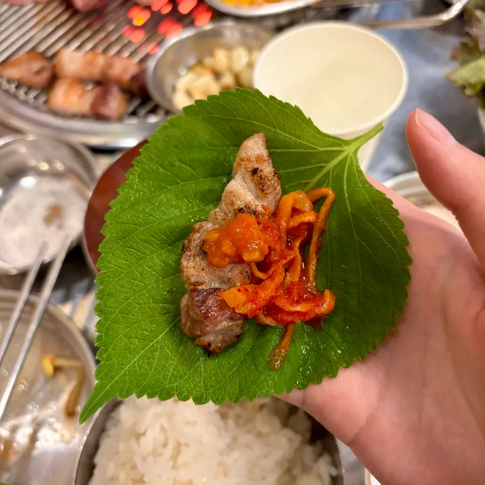 A bite of charcoal pork belly eaten together with radish salad