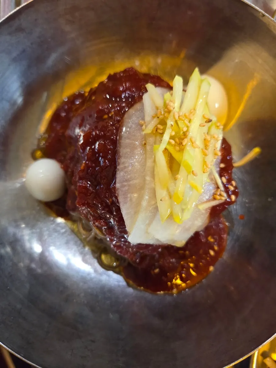 A piece of meat placed on top of the bibim naengmyeon