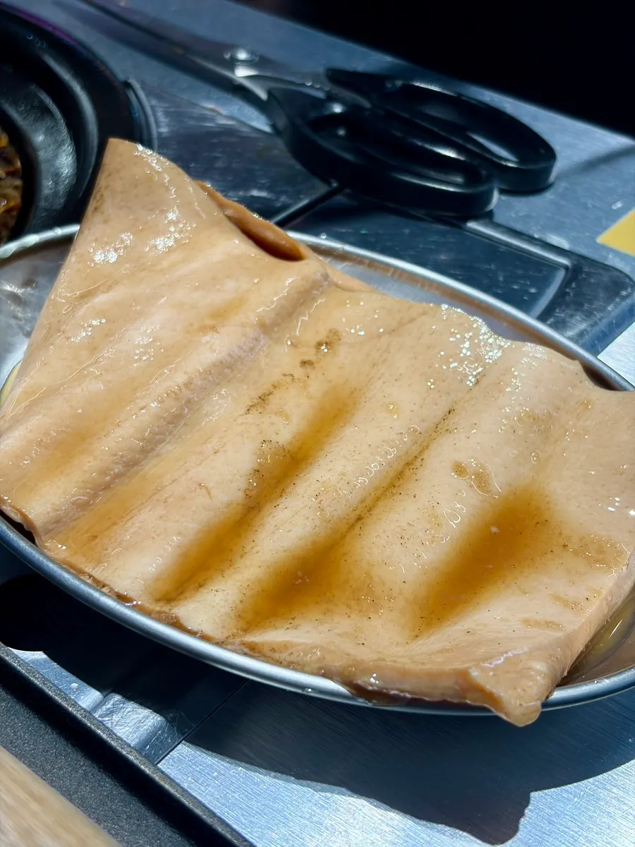 Pork skin being grilled with a pressing stone