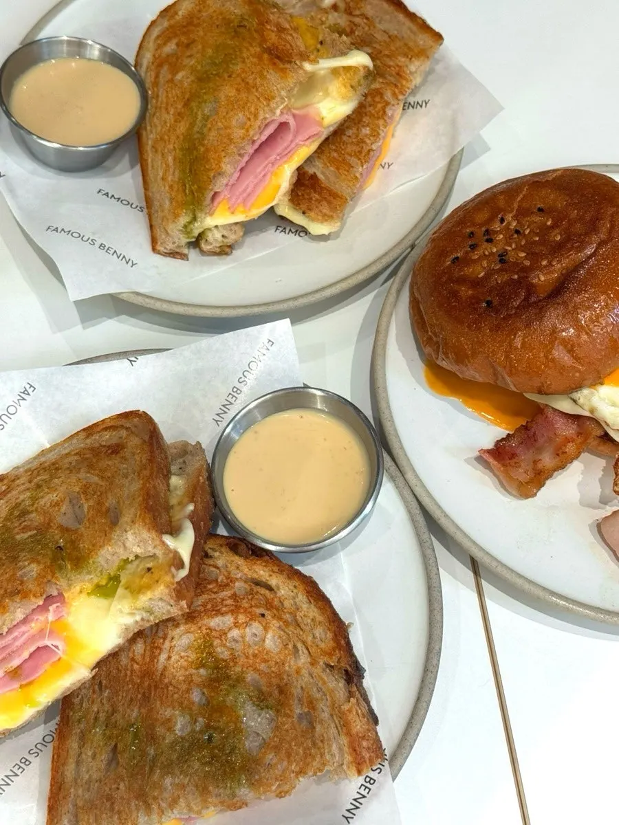 Table with ham cheese toast, bacon egg roll, and three drinks