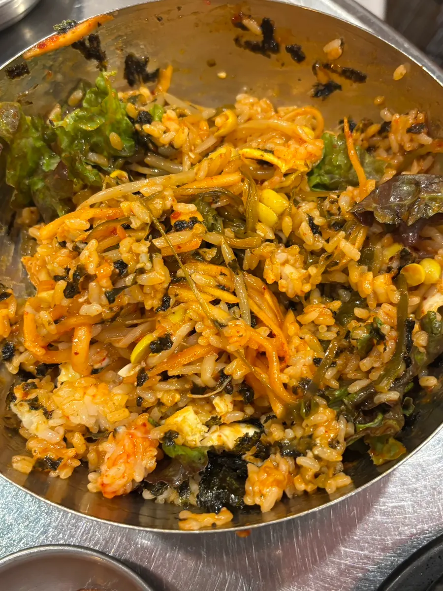 Bibimbap in a metal bowl topped with a soft fried egg