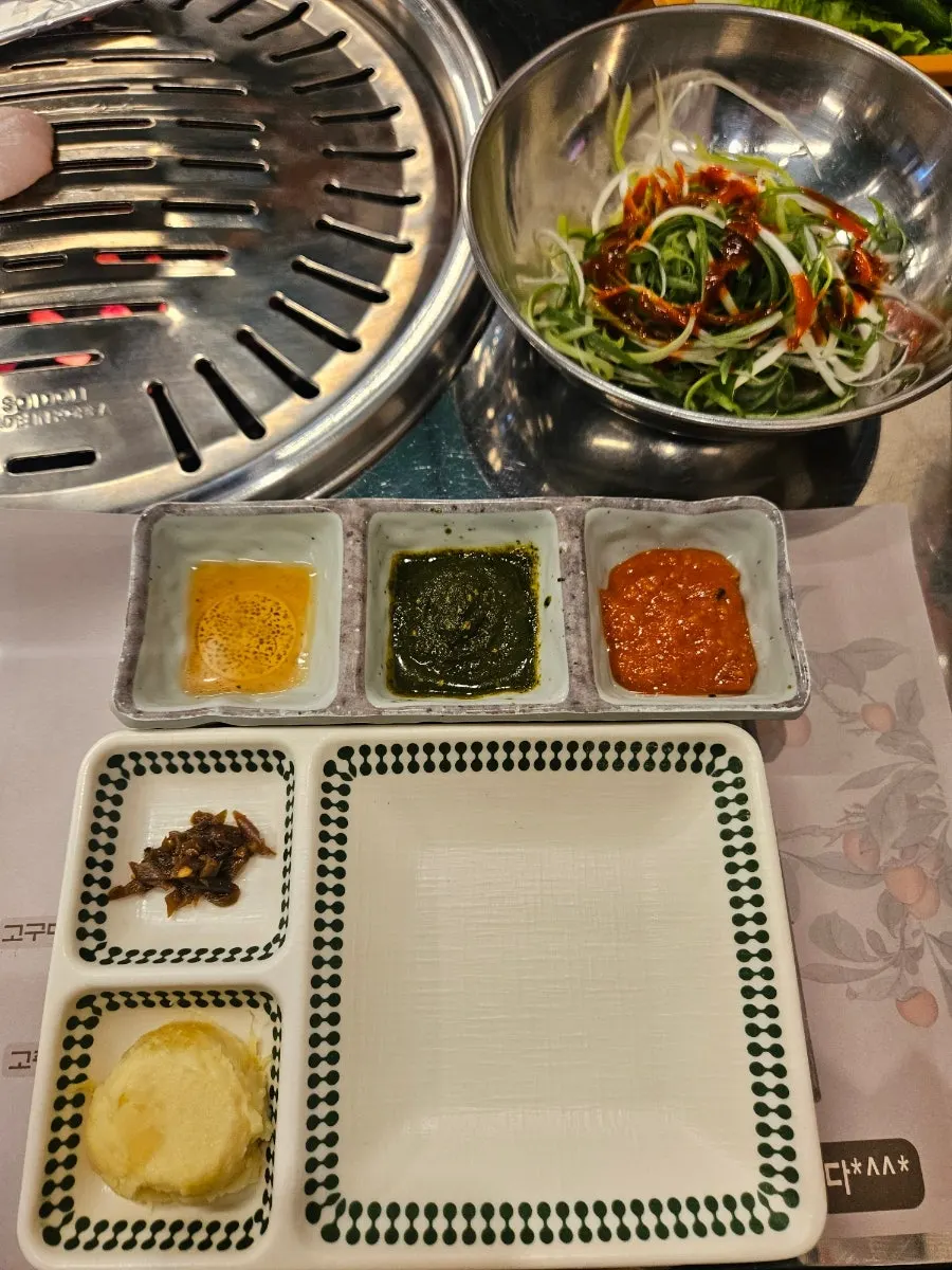 Table setting with potato salad, oil dipping sauce, basil sauce, and ssamjang side dishes