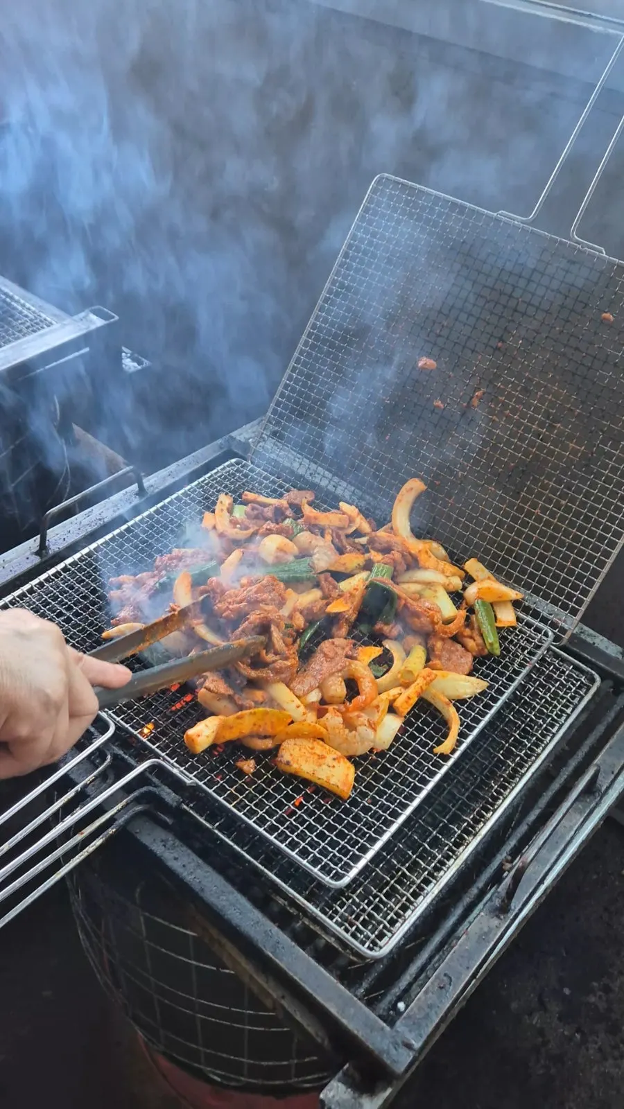 Duck jumulleok being pre-grilled on a grate over a charcoal drum