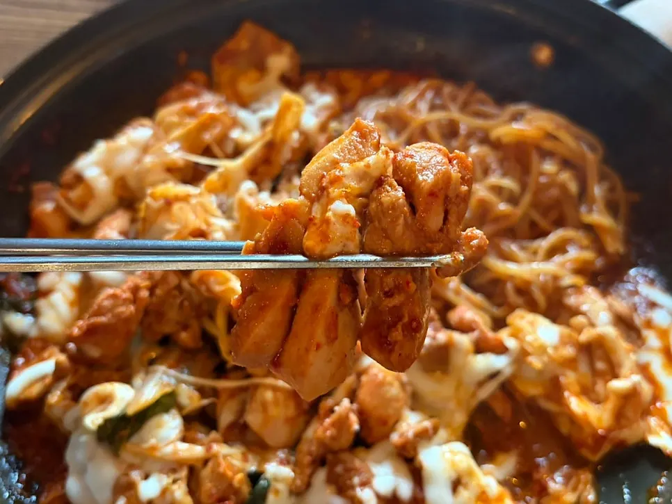 A stretch of melted cheese on a piece of cheese dakgalbi
