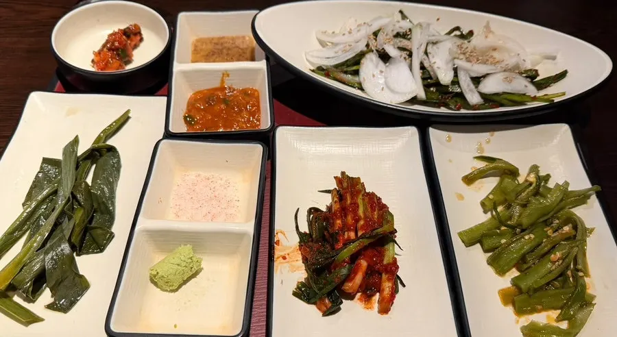 Basic banchan spread of green onion kimchi, chive salad, mountain garlic leaves and baek-kimchi