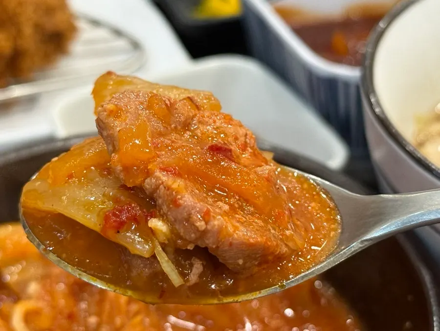 Scooping a spoonful of kimchi jjigae to eat with rice
