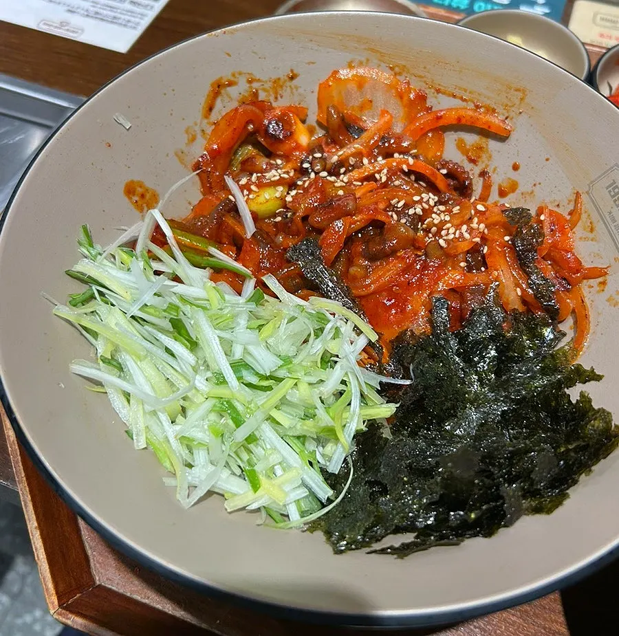Spicy octopus stir-fry rice bowl topped with shredded green onion and seaweed flakes