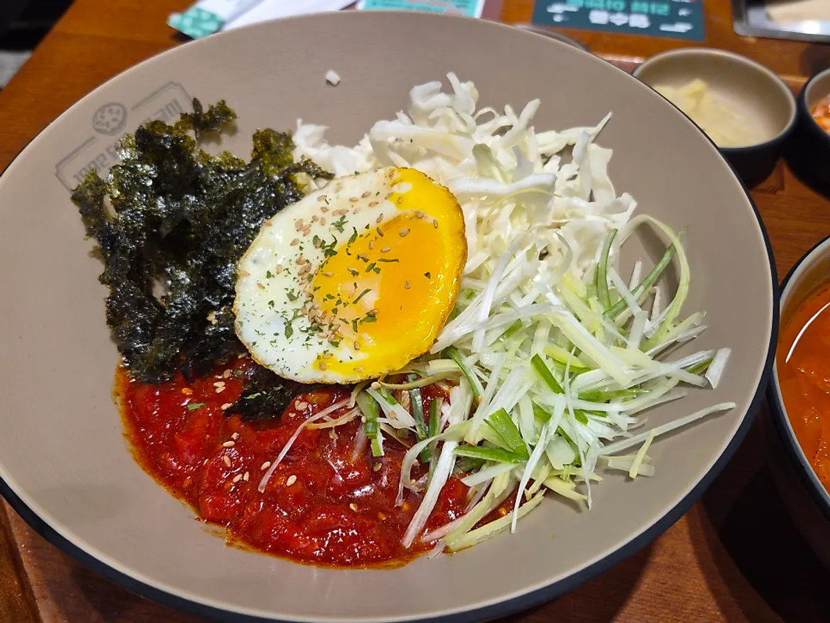 Yukhoe rice bowl topped with scallion strips, cabbage, and fried egg