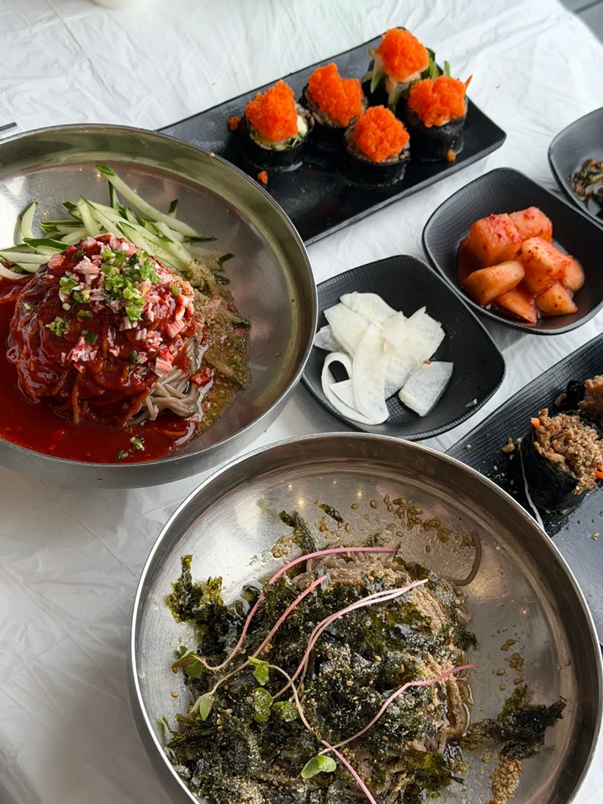 Table spread of spicy bibim makguksu, perilla oil makguksu, and buckwheat gimbap