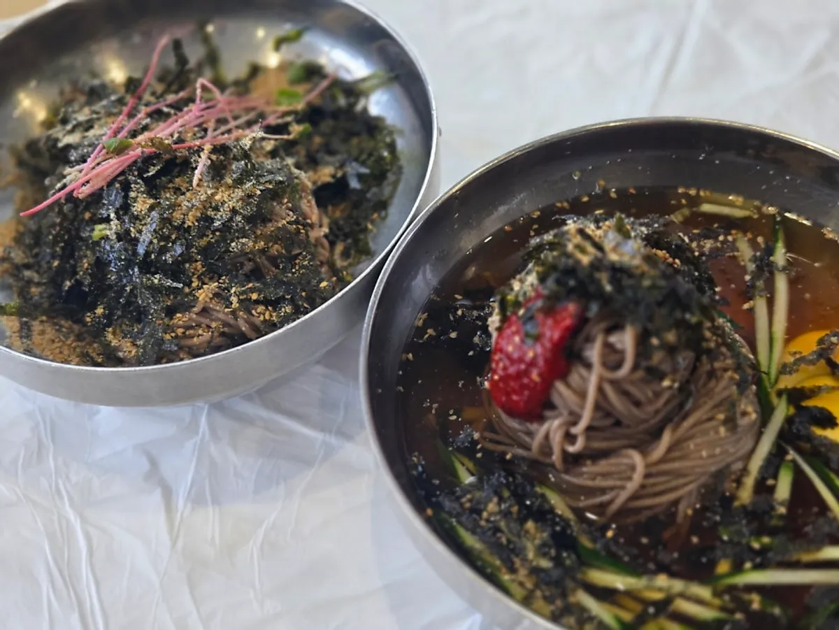 Two bowls of makguksu on a window table with the sea in the background