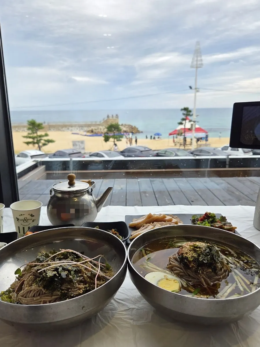 창가 자리에서 바다를 배경으로 놓인 막국수
