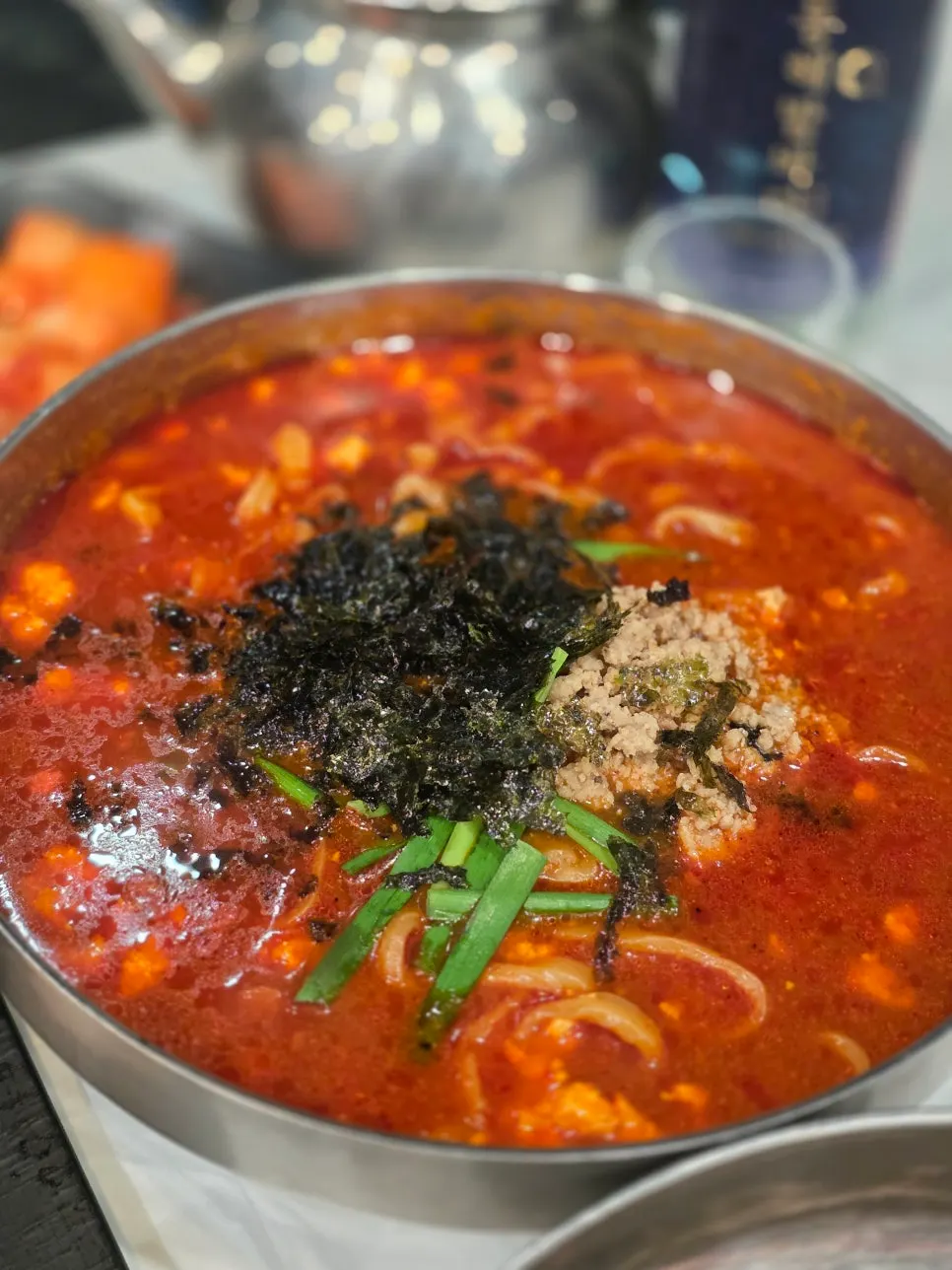 Spicy sundubu kalguksu topped with seaweed flakes and chives