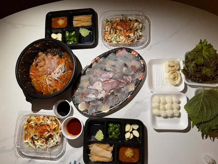 Assorted sashimi, mulhoe, and side dishes laid out on the hotel table