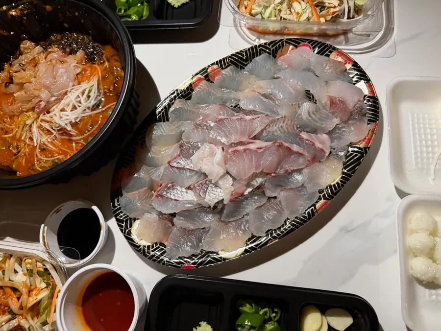 Sashimi, mulhoe, and side dishes each organized in their own containers