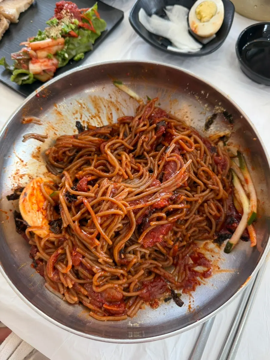 A bite of mixed makguksu topped with kimchi