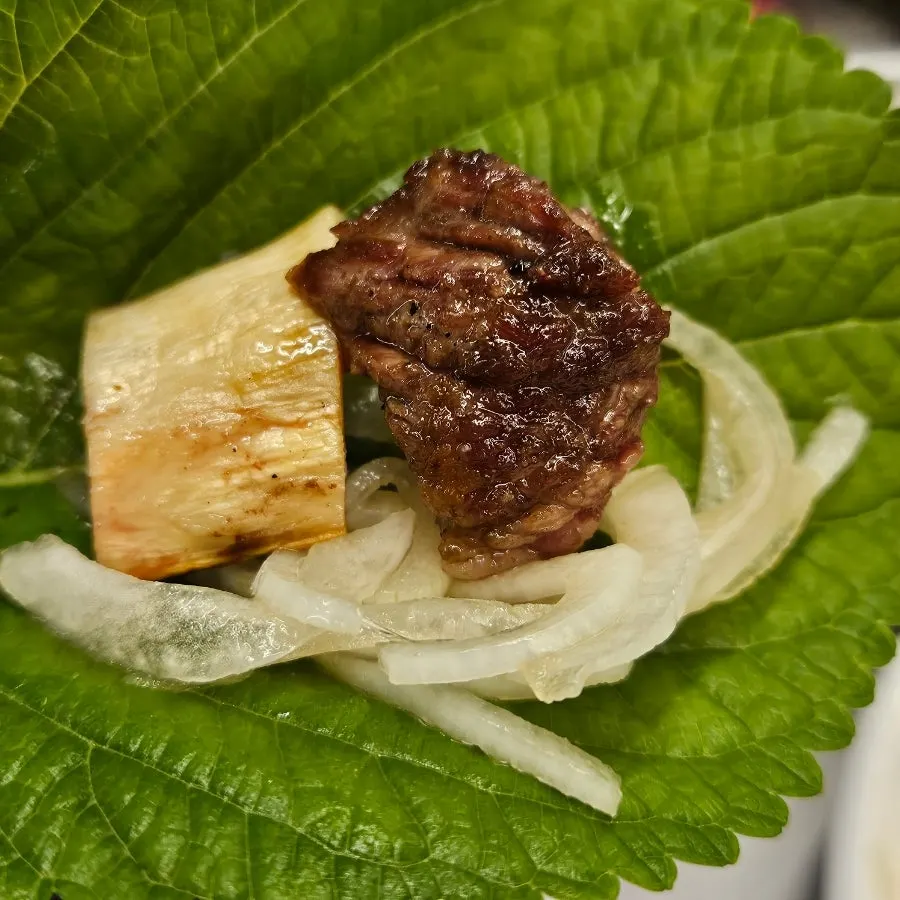 A bite of grilled woo-dae galbi with side dishes
