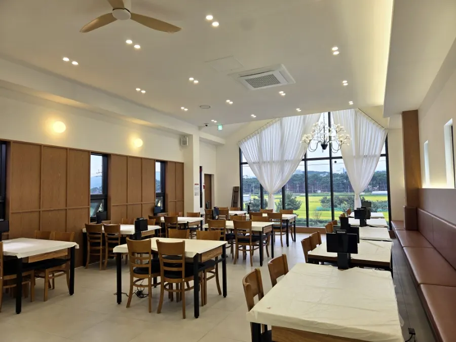 Sunlit second-floor dining hall at Gangneung Jeonbok Haenyeo Village with floor-to-ceiling windows