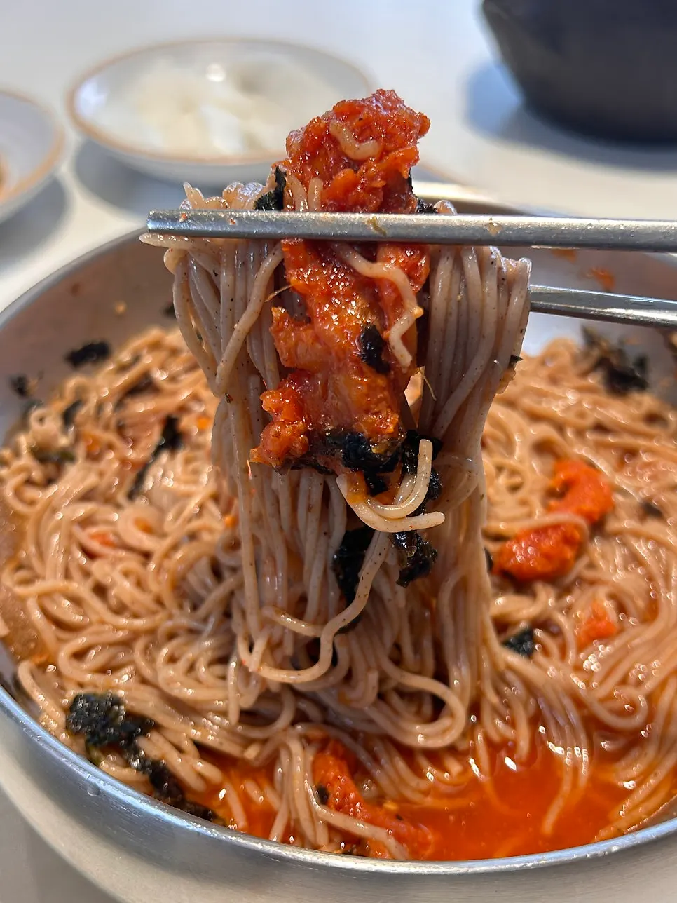 Buckwheat noodles lifted from a bowl of dongchimi makguksu