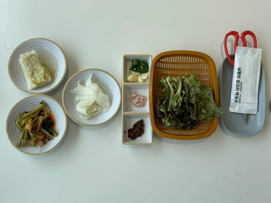 Table set with three side dishes — young radish greens, baek-kimchi, radish — and wrap vegetables