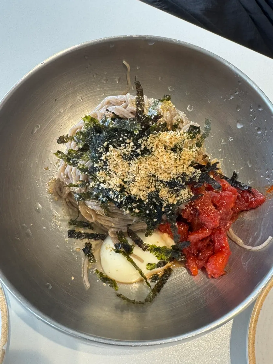 Pollack sashimi makguksu topped with seaweed flakes, sesame seeds, and boiled egg