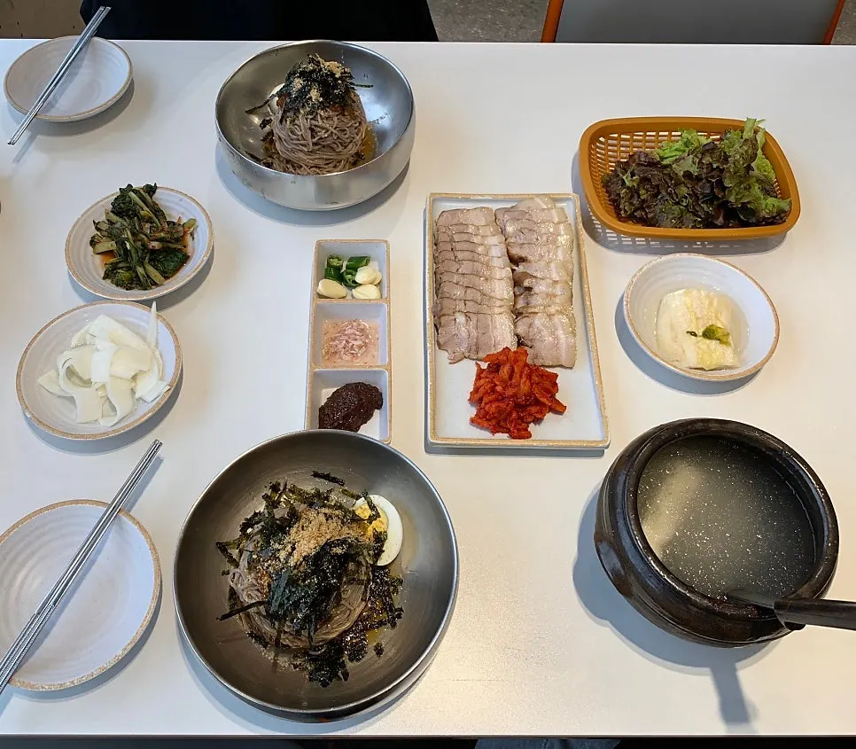 Two bowls of dongchimi makguksu with a small sujuk platter on the table