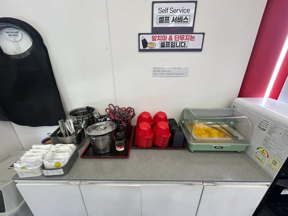 Self-service corner with pickled radish, aprons, and tongs