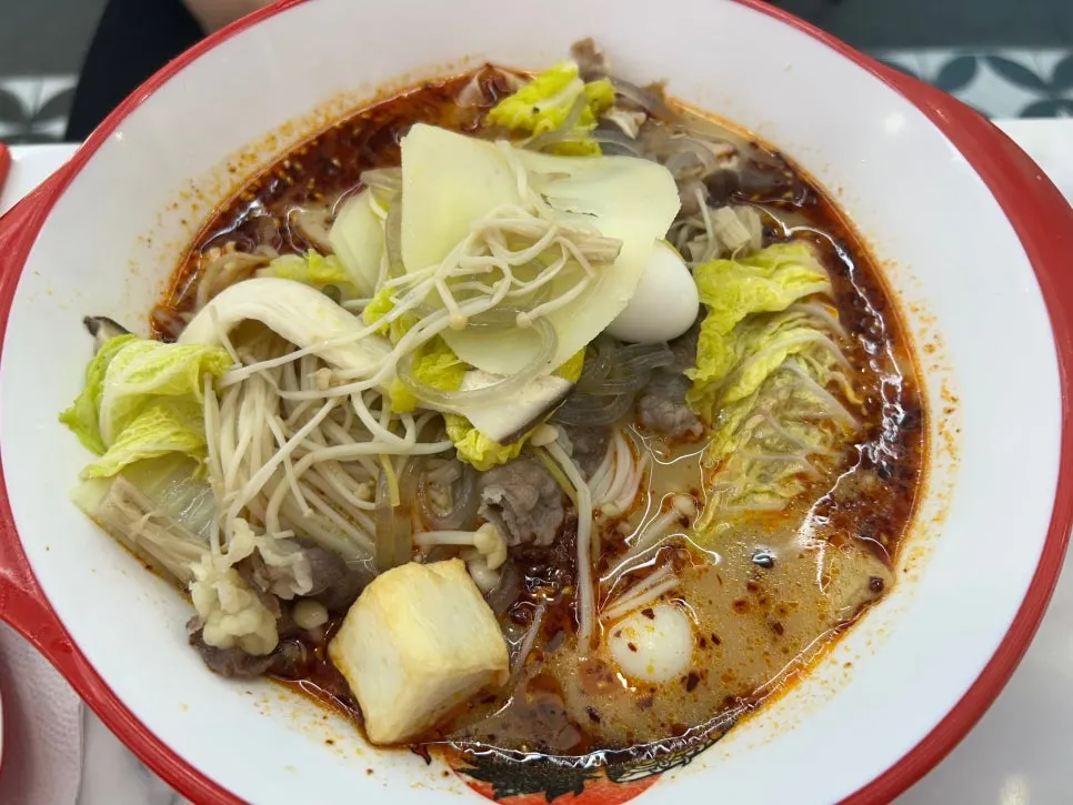 A bowl of malatang with napa cabbage, enoki mushrooms, potato, and tofu skin