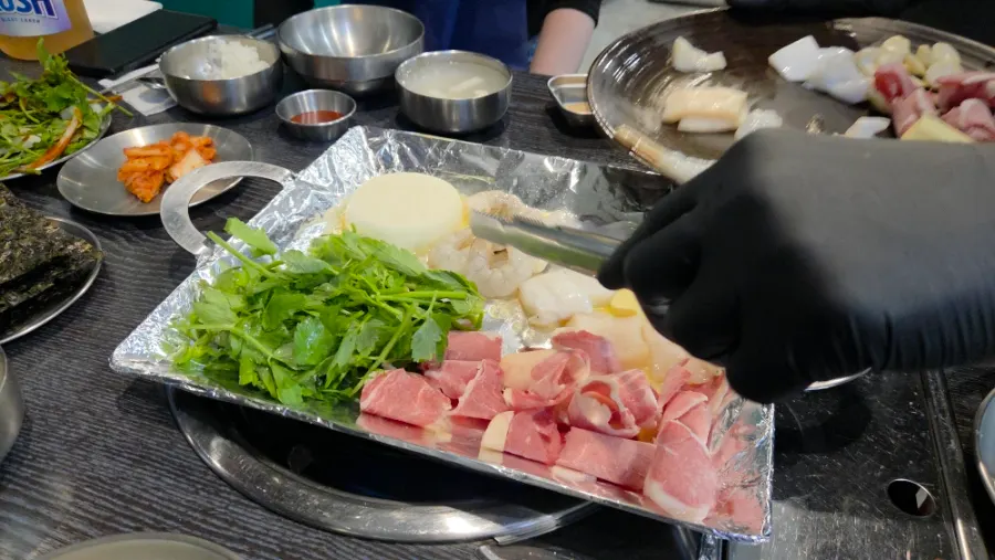 Staff member grilling the seafood-and-meat set on the hot plate
