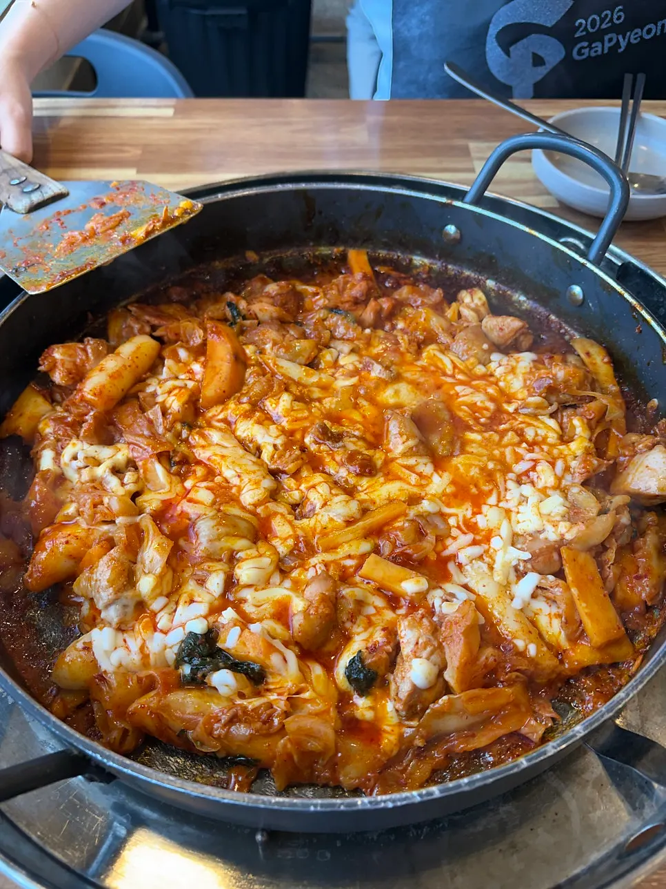 The dakgalbi pan being stirred with a spatula as the cheese melts