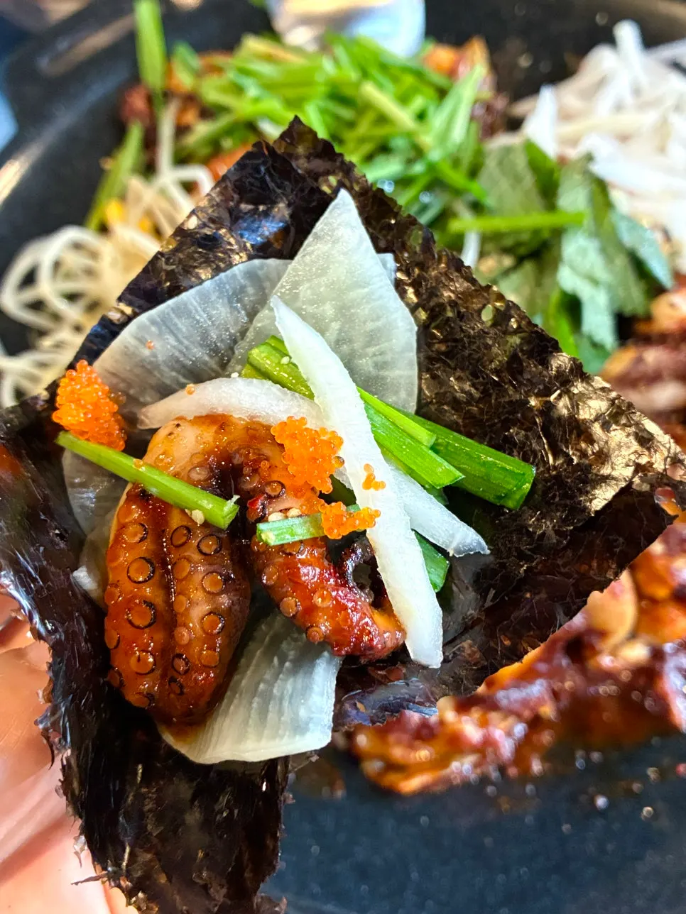 Jjukkumi wrap with pickled radish and flying fish roe on a perilla leaf