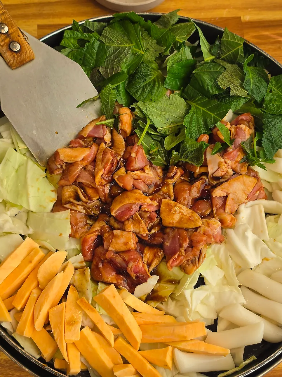 Soy sauce dakgalbi on the hot plate with perilla leaves and sweet potato
