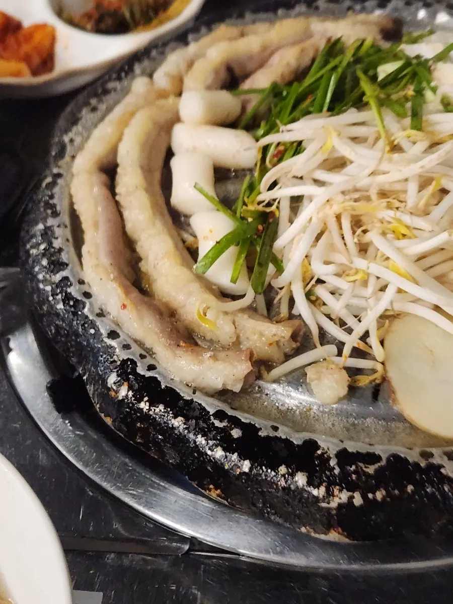 Grill with gopchang cooking alongside bean sprouts, potato, and napa cabbage
