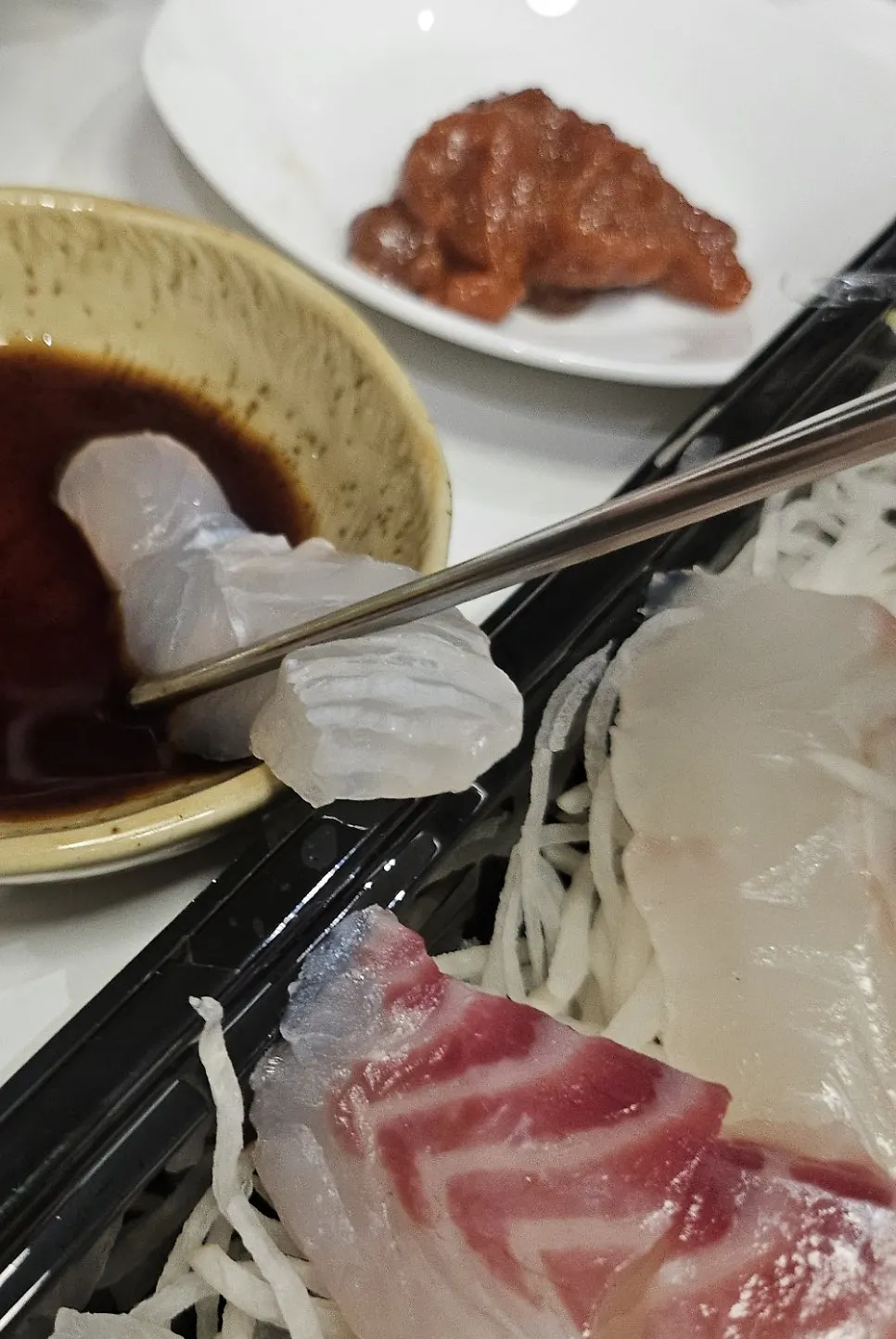 A piece of sashimi lifted with chopsticks alongside radish sprouts