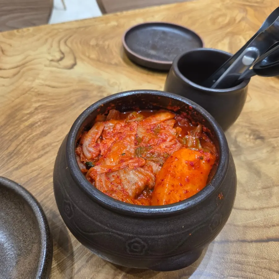 Well-fermented kimchi served in a mini jar with scissors and tongs