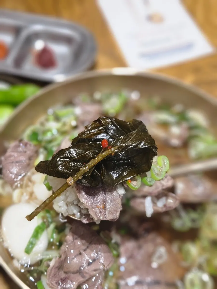 A spoonful of gomtang with banchan on the side