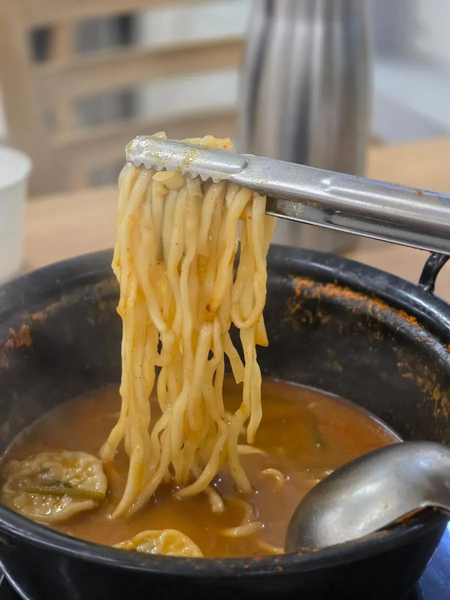 Kalguksu noodles being stirred and cooked in the broth