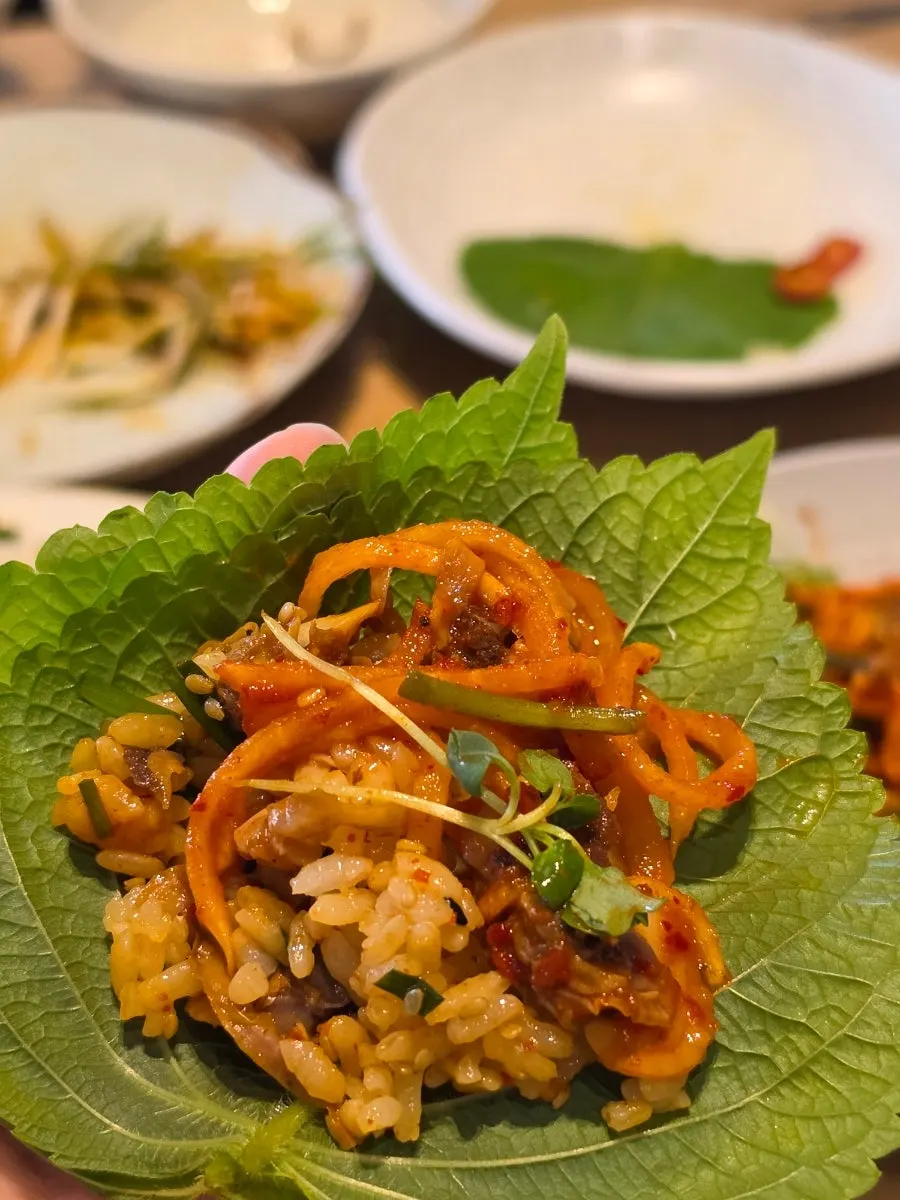 A perilla leaf wrap with cockle bibimbap and cockle salad on top