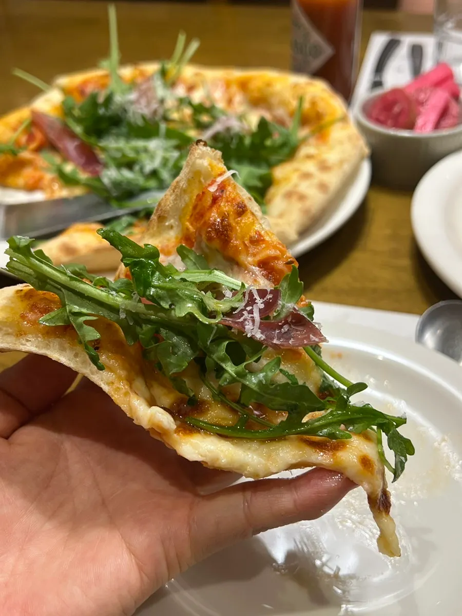 A pizza slice topped with prosciutto and arugula