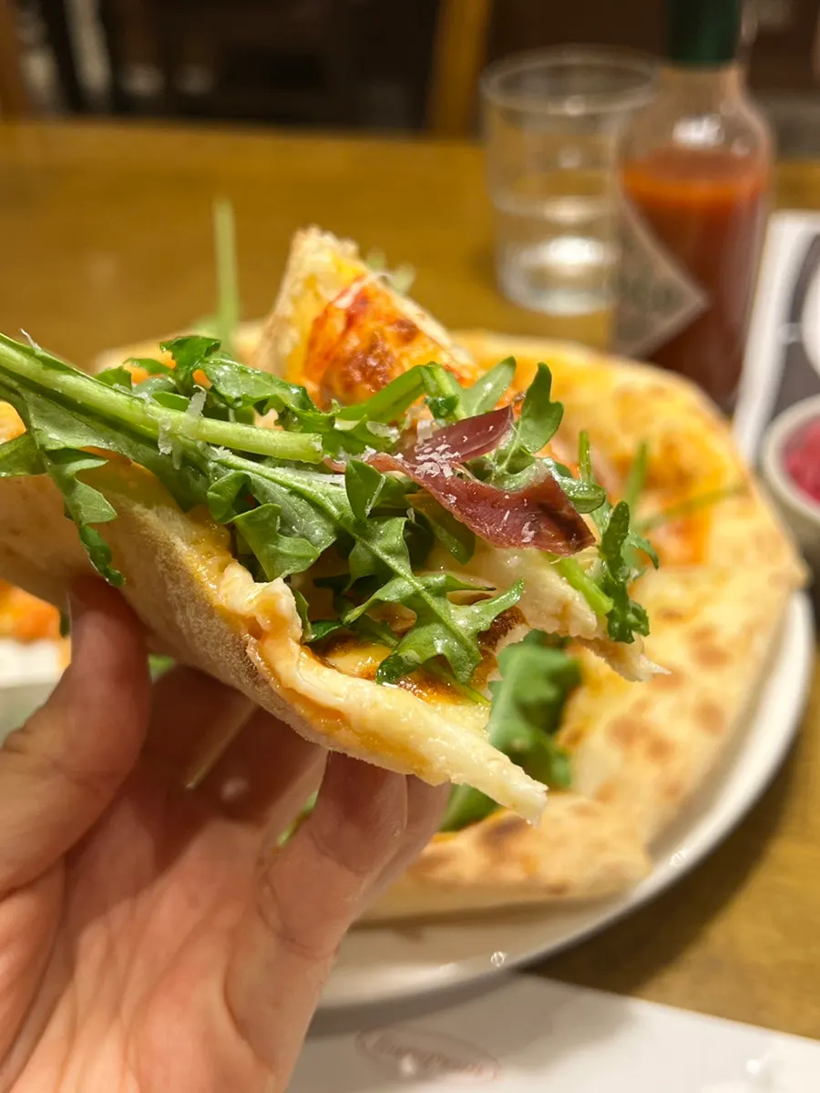 A slice of arugula prosciutto pizza being lifted