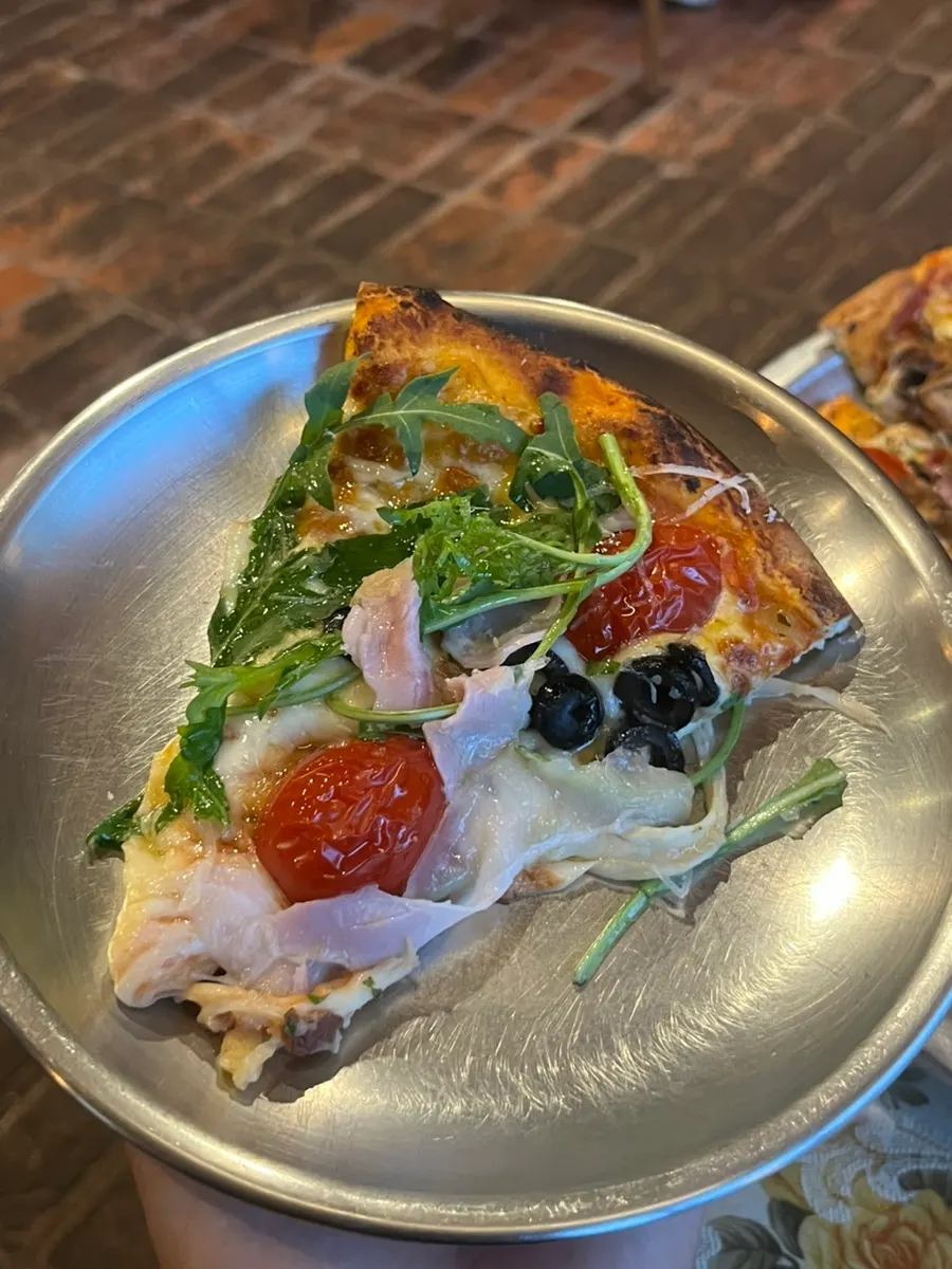 A slice lifted from the Jeju jambon arugula pizza