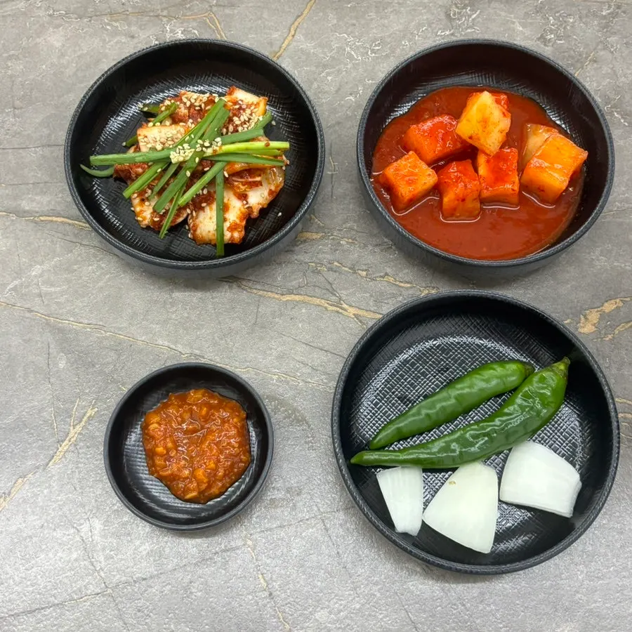 Table set with kimchi, kkakdugi, chili peppers, onion, and ssamjang