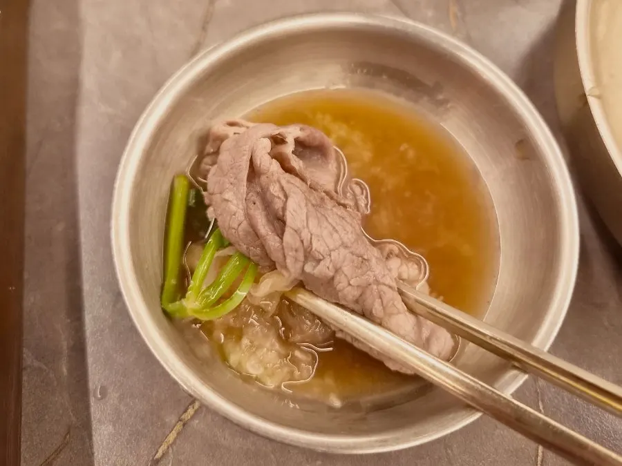 將涮涮鍋肉片放入高湯中的場景
