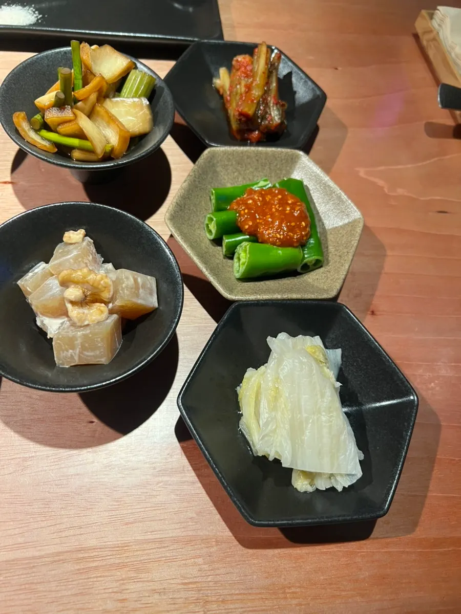 Side dish spread of cucumber peppers, pickles, gat kimchi, baek kimchi, and konjac salad