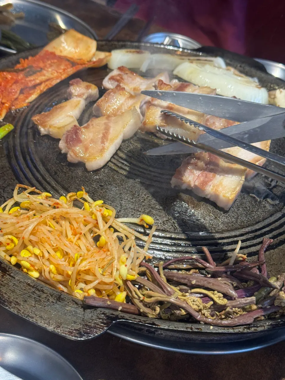 Raw pork belly grilling to a golden brown on the cauldron lid
